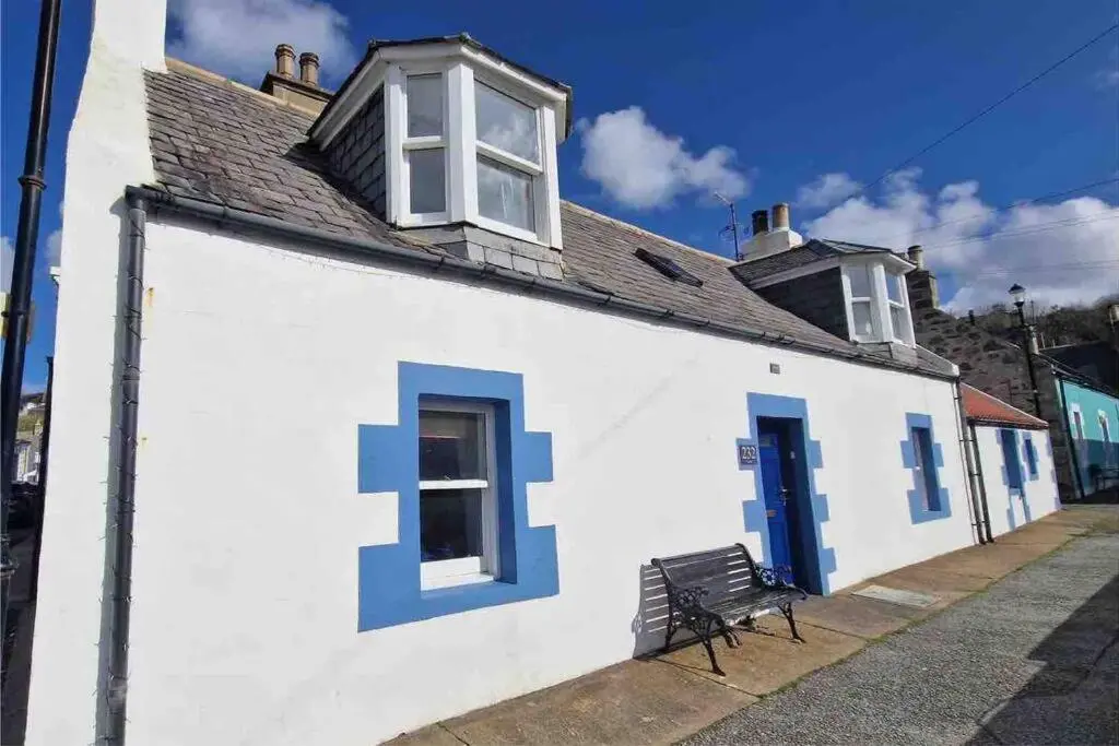 a white building with blue doors and a bench at Cullen Seaside Cottage in Cullen