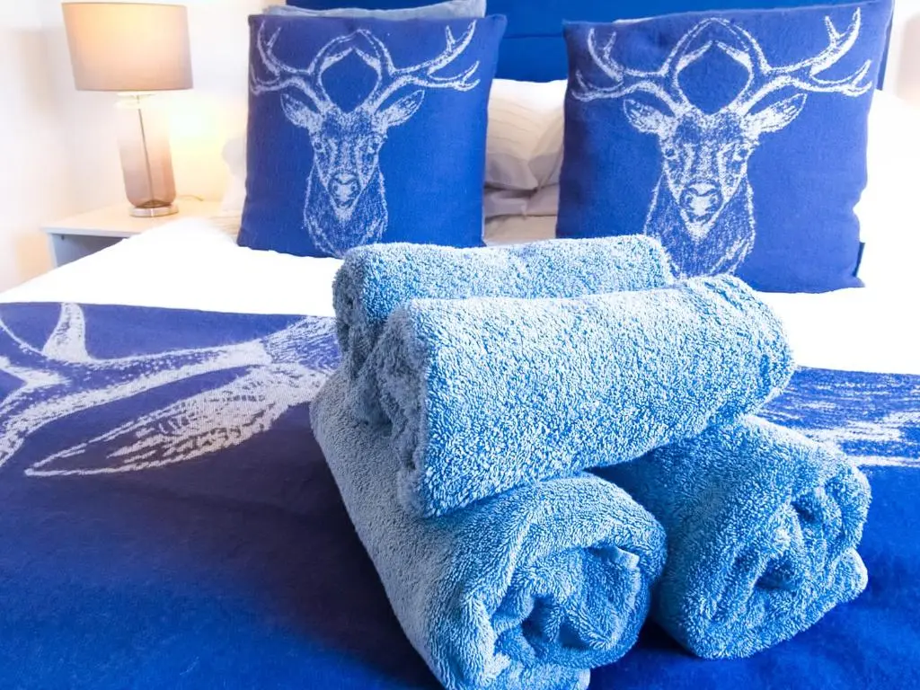 a bed with blue towels on it with two deer pillows at 26 Ben Avon in Aviemore