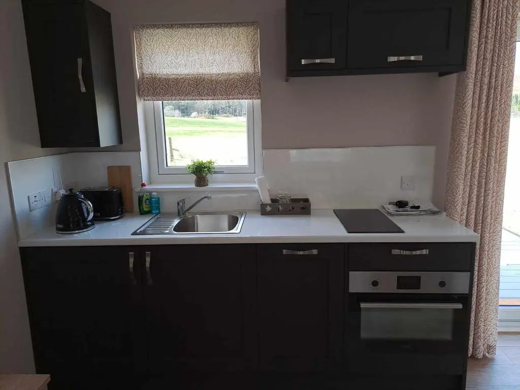 a kitchen with black cabinets and a sink and a window at Rowan Bank Retreat in Fort Augustus