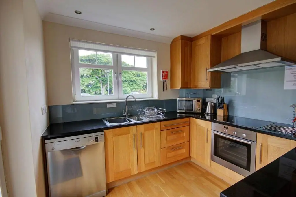 a kitchen with wooden cabinets and a sink and a window at No1 The Links Apartment, Brora in Brora