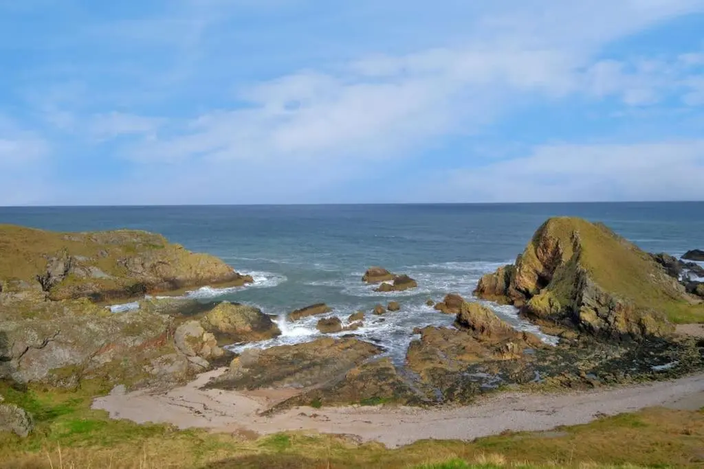 a beach with some rocks and the ocean at Cliff Top Cottage with Sea Views in Portknockie