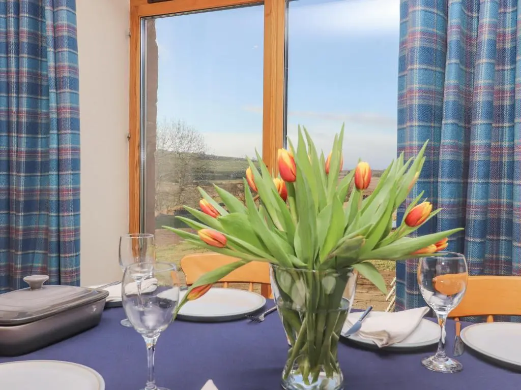 a table with a vase of tulips on it at Reyflat Barn in Fortrose