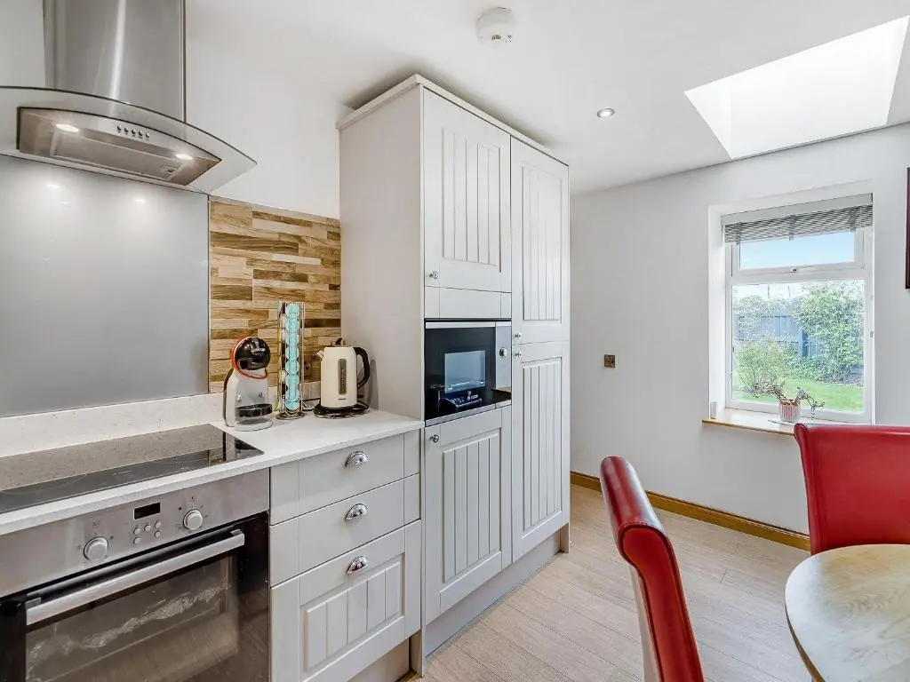a kitchen with white cabinets and a red chair at Mains Of Durn Cottage, in Banff
