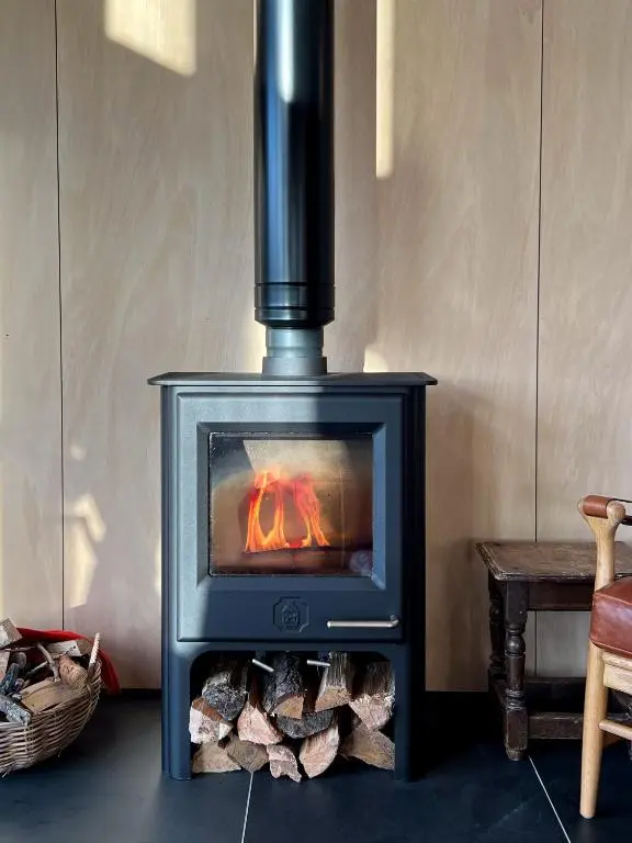 a wood stove with a fire in a room at Tillyfruskie Farm Holiday Cabin, Finzean in Banchory