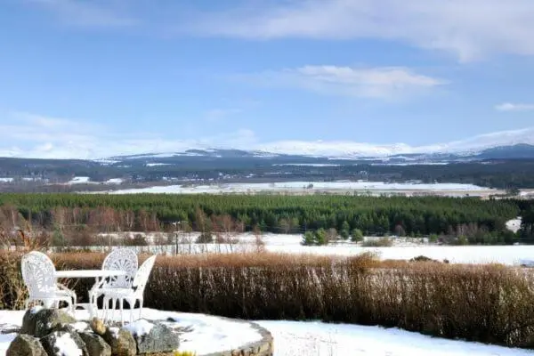 two chairs and a table with a view of a snow covered field at Beautiful Lodge with hot tub & panoramic views in Boat of Garten