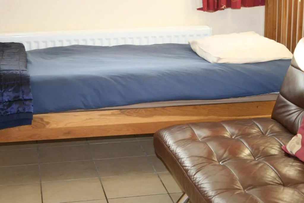 a bed with a blue blanket and a leather couch at BCC Loch Ness Hostel in Bearnock