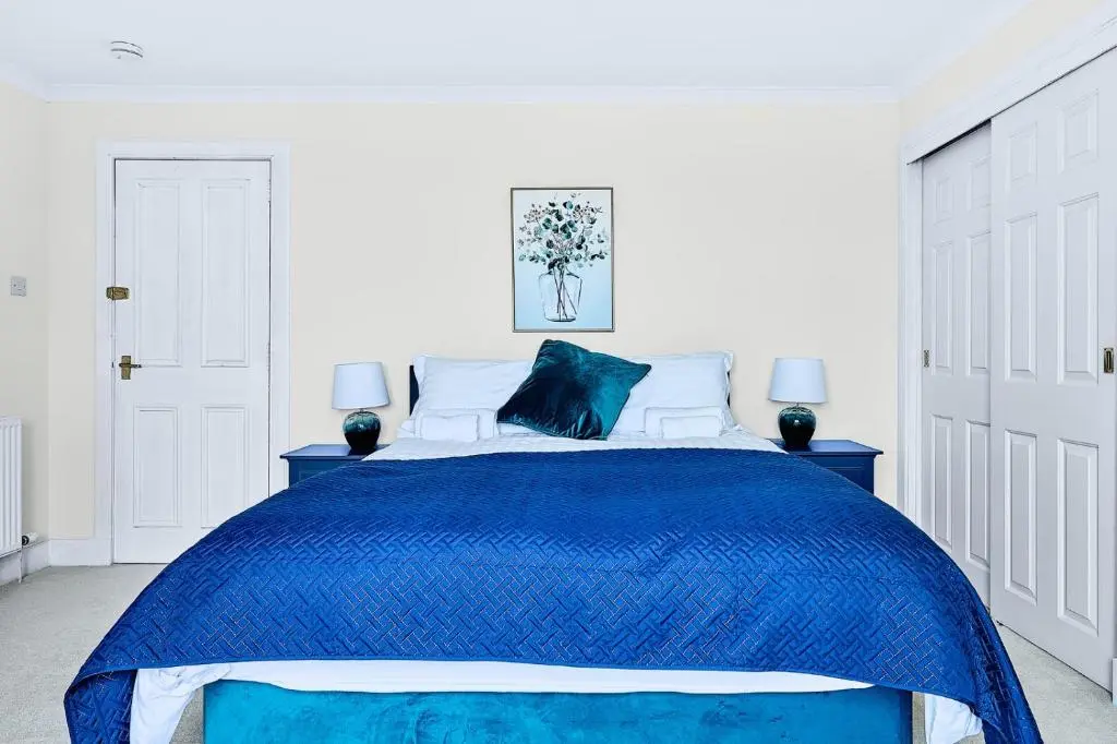 a bed with a blue comforter in a white bedroom at Kinkell House Rooms in Cononbridge