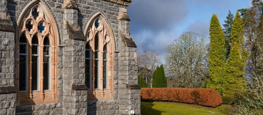 an old stone building with a window and bushes at Abbey Holidays Loch Ness Luxury Self Catering 2 Bedroom Cottages in Fort Augustus