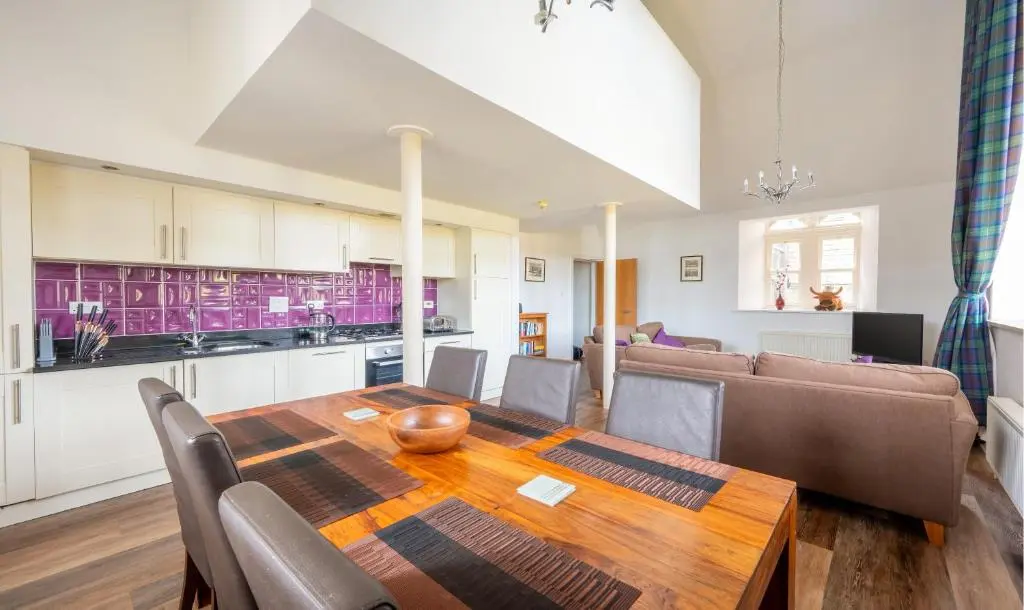 a kitchen and living room with a wooden table and a couch at The Caledonian 3 Bedroom Self Catering Apartment in historic Abbey in Fort Augustus