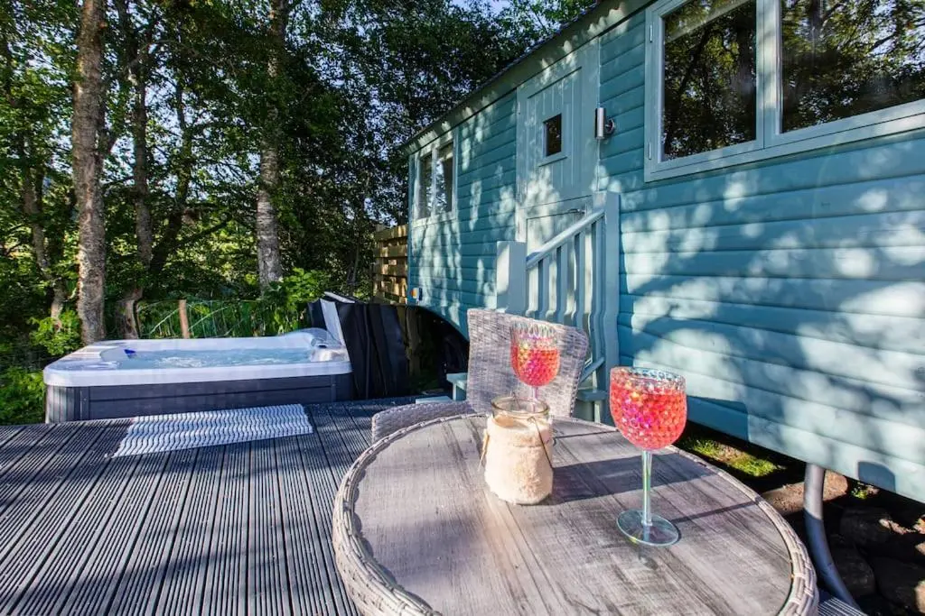 a wooden table with two wine glasses on a patio at Cosy Shepherds Hut with hot tub in the Scottish Highlands in Stittenham