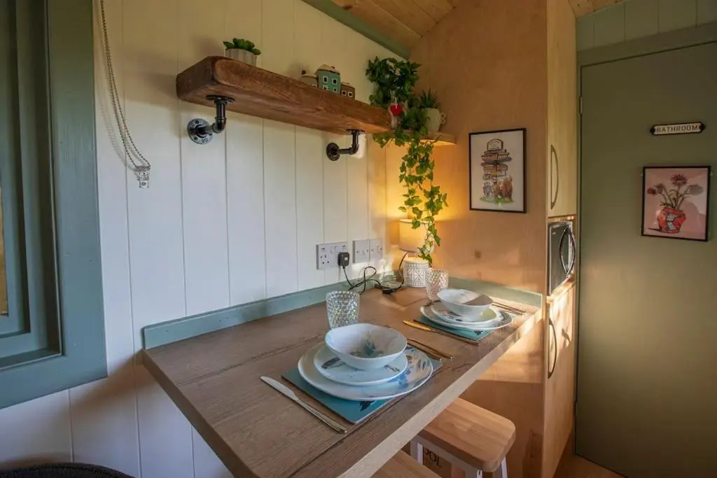 a kitchen with a table with plates and a refrigerator at Cosy Shepherds Hut with hot tub in the Scottish Highlands in Stittenham