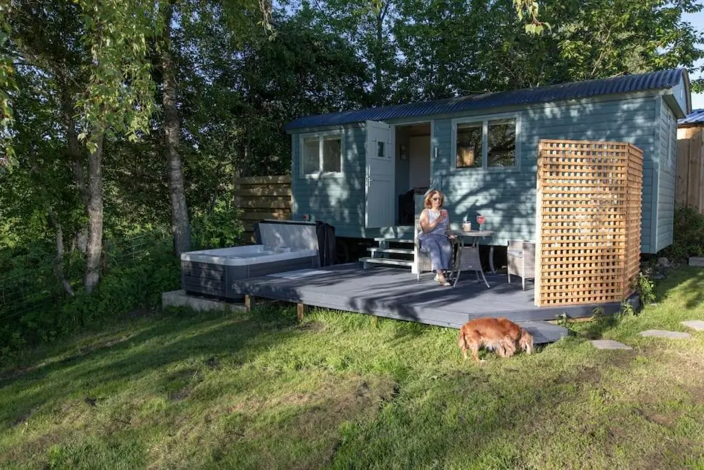 a woman standing in front of a tiny house with a dog at Cosy Shepherds Hut with hot tub in the Scottish Highlands in Stittenham