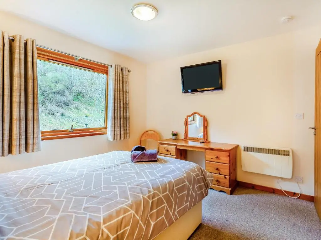 a bedroom with a bed and a desk and a television at Balnagowan Mill in Nethy Bridge
