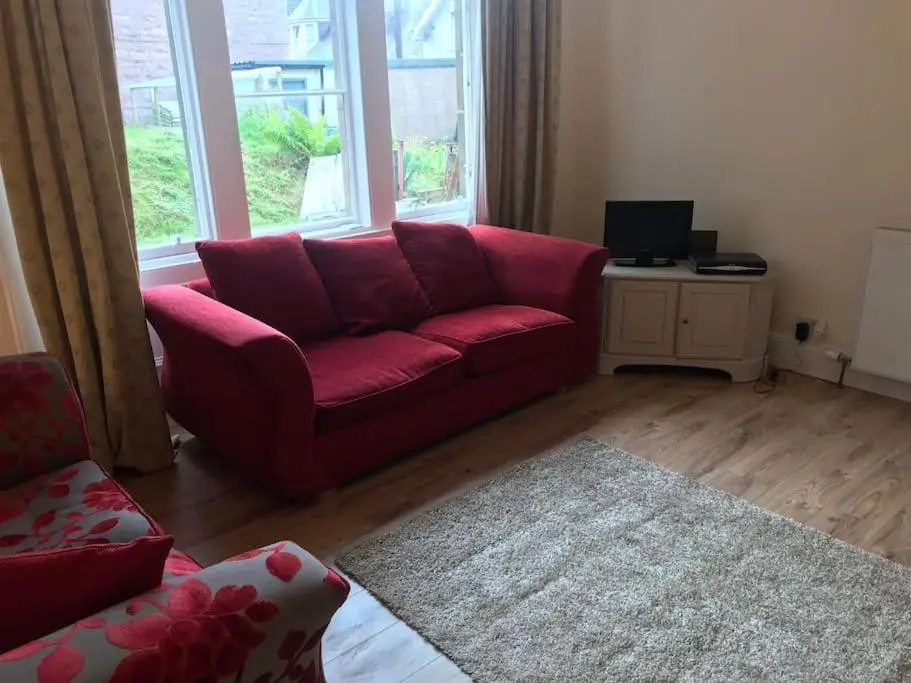 a living room with a red couch in front of a window at Heather House, beautiful family home, sleeps 8 in Inverness