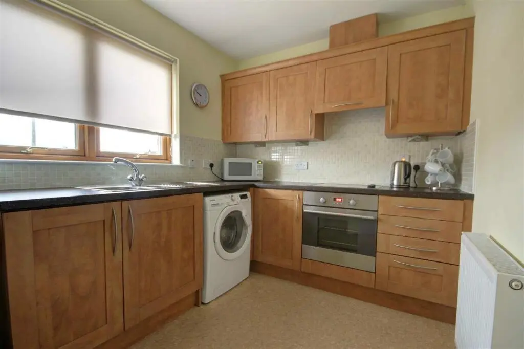 a kitchen with wooden cabinets and a washing machine at The Old Mill Apartment, on NC500 in Brora