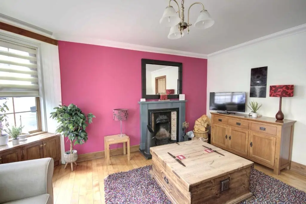 a living room with pink walls and a wooden coffee table at The Apartment at Allt-Sagart in Golspie