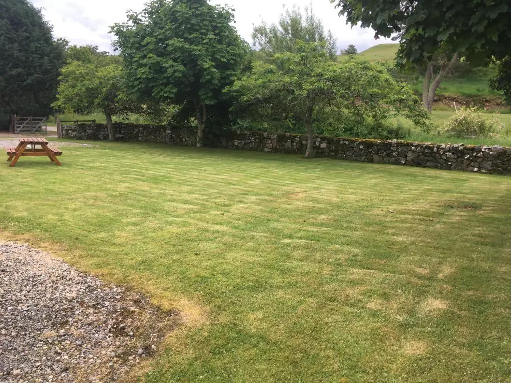a grassy yard with a picnic table and a stone wall at Ruthven House Holiday Cottages in Kingussie