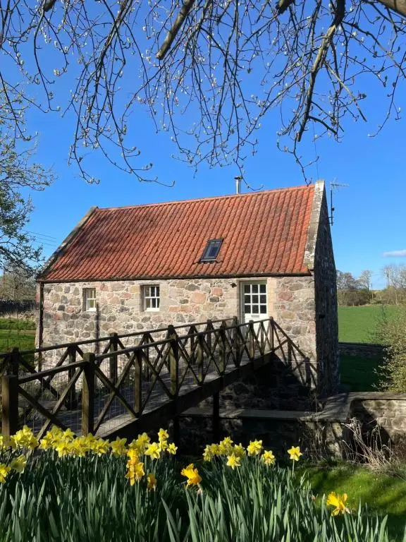 an old stone house with a red roof and a wooden bridge at Stunning Rural Mill House nr beach and harbour in Banff