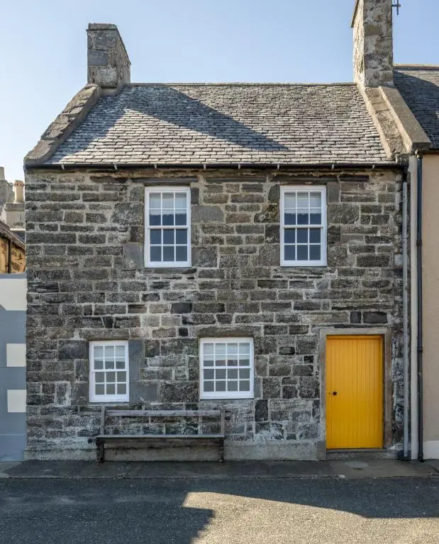 a brick house with a yellow door and a bench at 6 Shorehead, Portsoy in Portsoy
