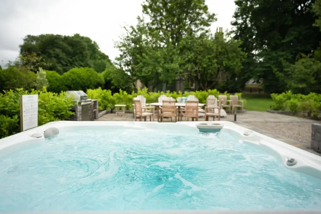 a hot tub in a yard with chairs and tables at The Dell of Rothiemurchus - Seasgair Lodges in Aviemore