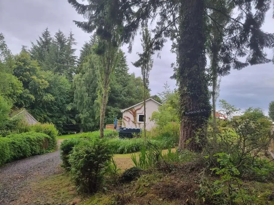 a house in the middle of a yard with trees at Rowanlea Cottage in Inverness