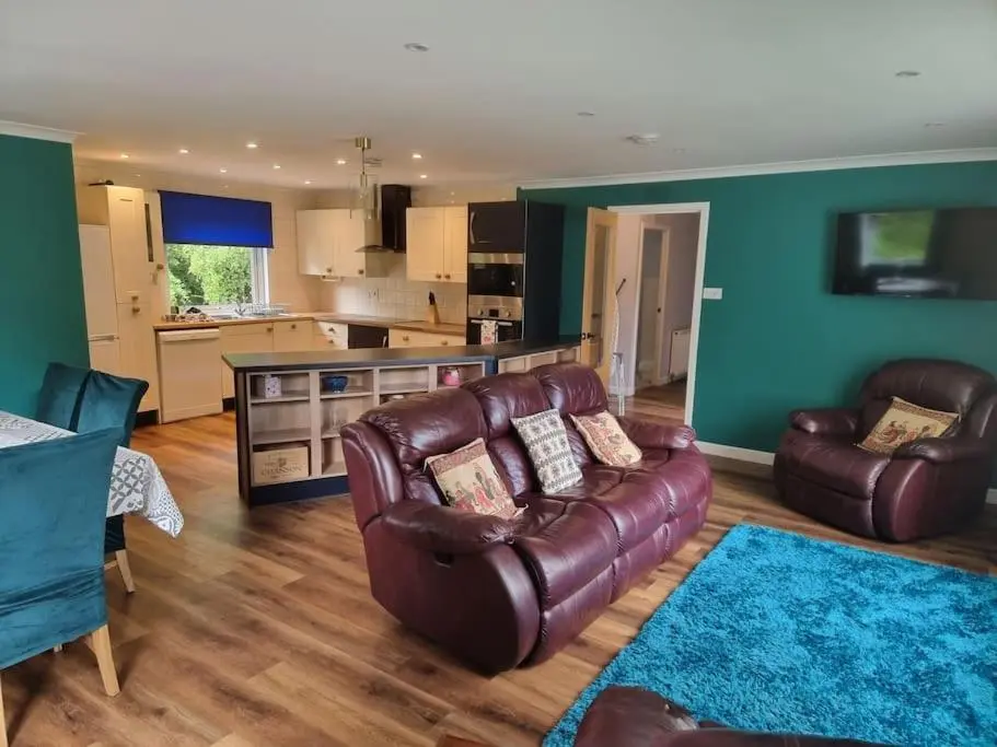 a living room with a leather couch and a kitchen at Rowanlea Cottage in Inverness