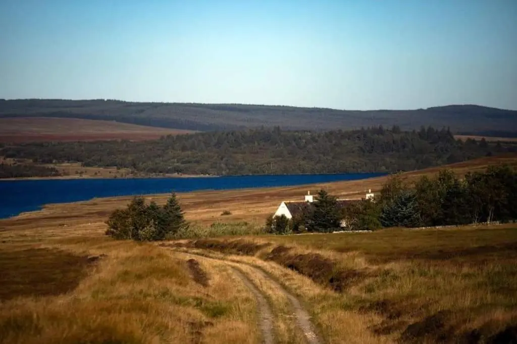 a field with a barn in the middle of a lake at Torran Cottage - Views, Exclusivity & Tranquility in Halkirk