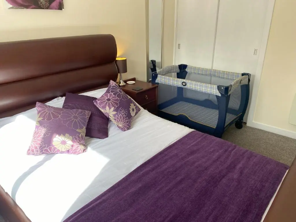 a bedroom with a bed with purple sheets and a crib at Treetops - Bright 2 Bed Flat - Super Location in Inverness