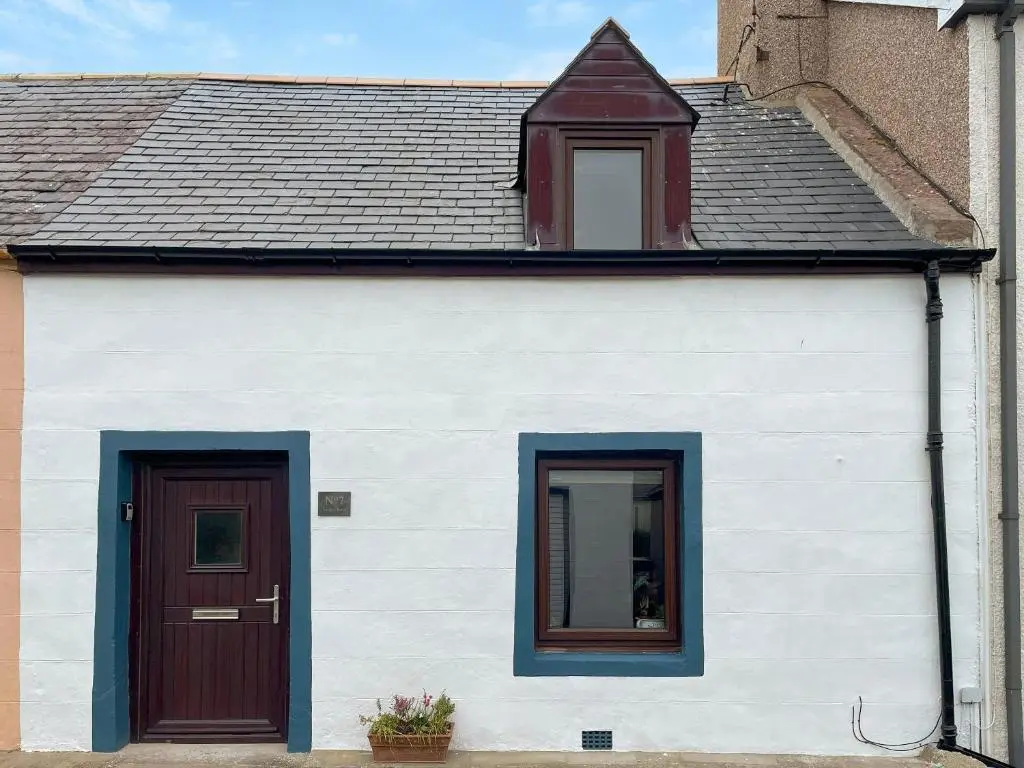 a white house with a red door and two windows at The Wee Belter in Dornoch