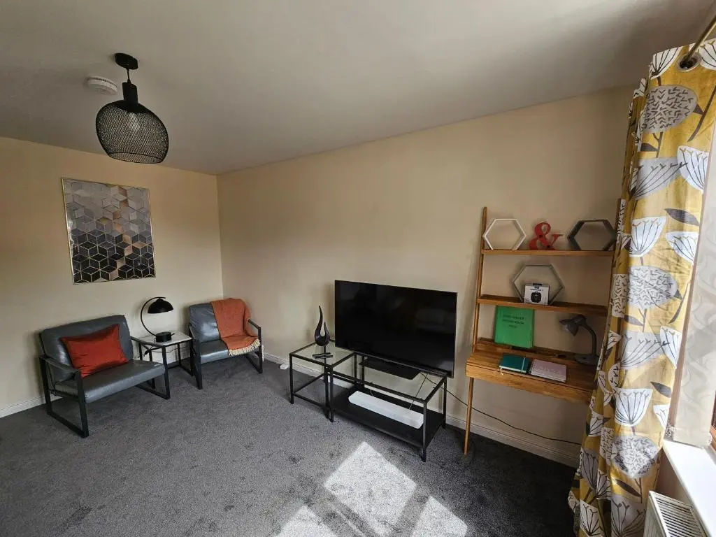 a living room with a flat screen tv and chairs at Modern Dornoch Apartment in Dornoch