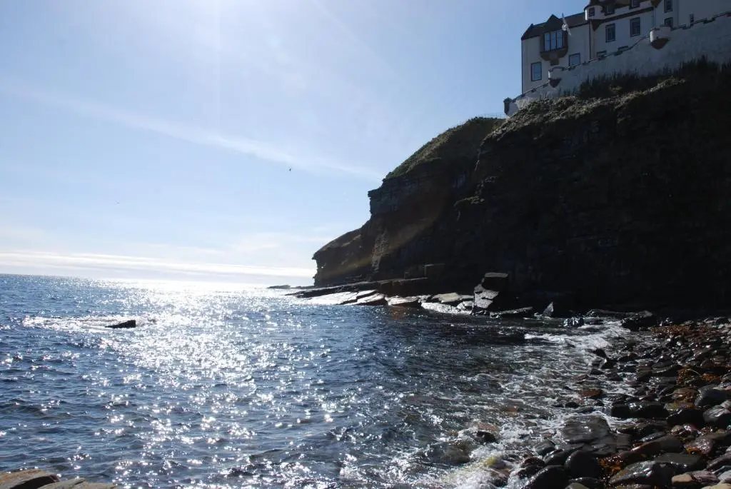 a rocky beach with a building on the side of a cliff at Faodail 'a lucky find' in Dunbeath