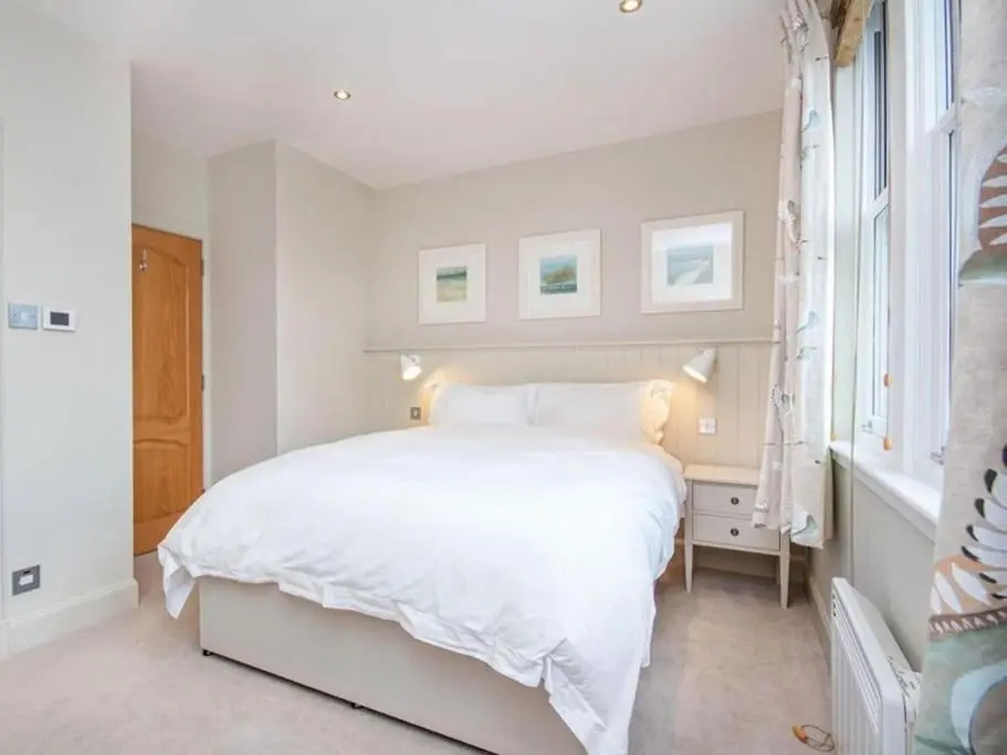 a white bedroom with a white bed and a window at Townhouse on the Square, Dornoch in Dornoch