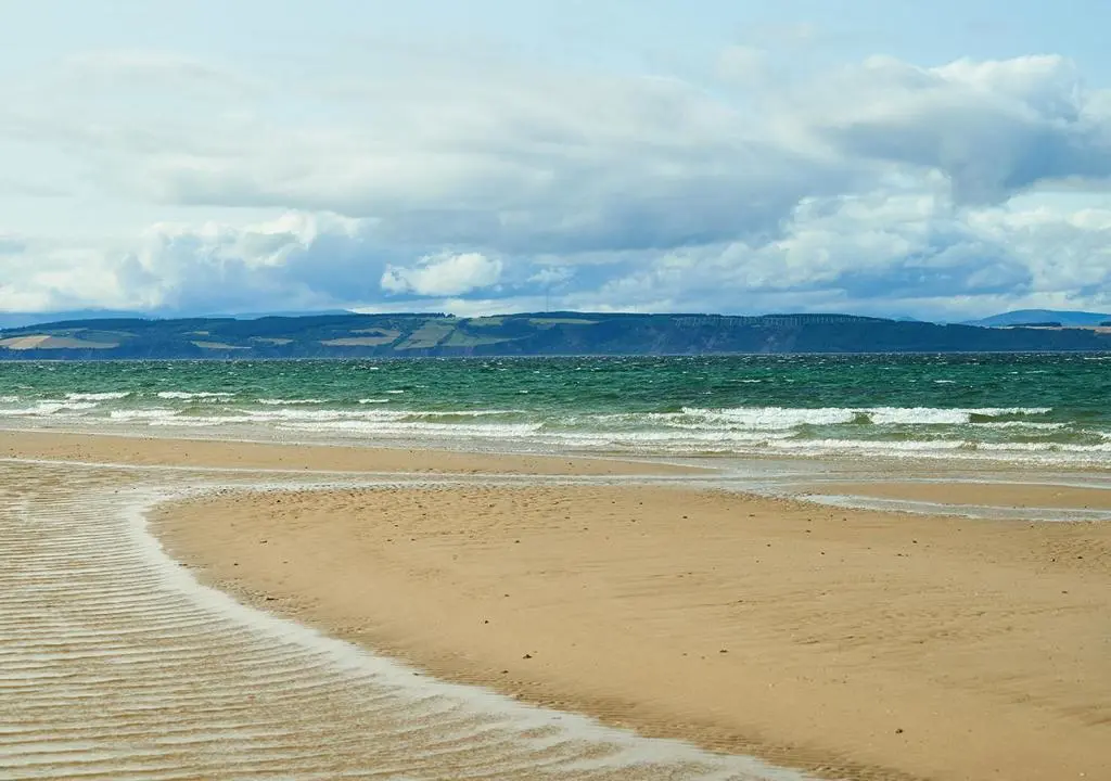 a sandy beach with waves in the ocean at Golf View Hotel & Spa in Nairn