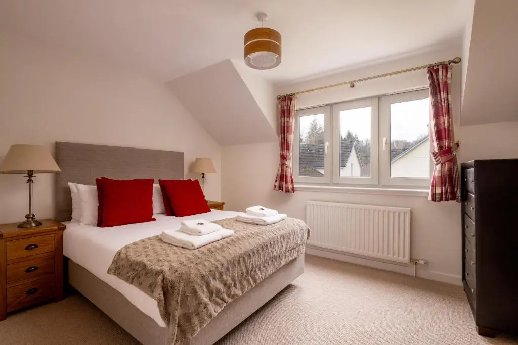 a bedroom with a bed with red pillows and a window at Courtyard Cottage 3, Riverside Cottage in Fort Augustus