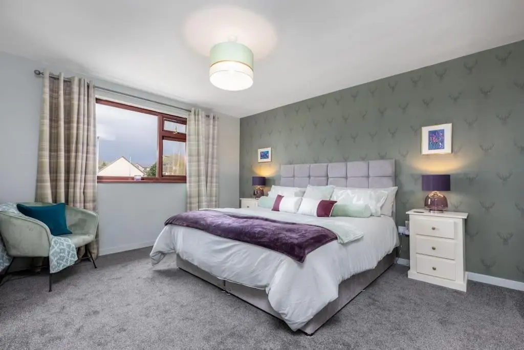 a bedroom with a large bed and a chair at Orcadia Sutherland Road Dornoch IV25 3SX in Dornoch