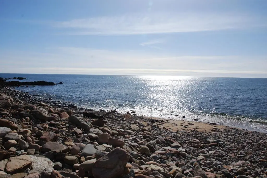 a rocky beach with the sun reflecting on the water at Camhanaich 'Half light of dawn' in Dunbeath