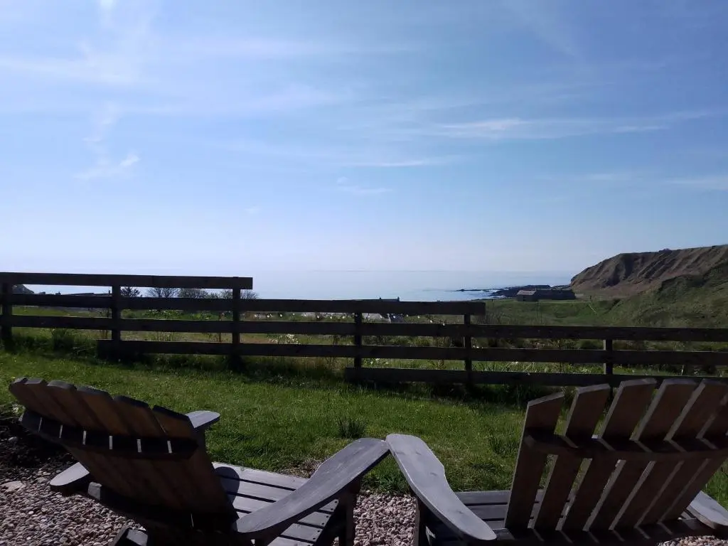 two chairs sitting on the grass near the ocean at Camhanaich 'Half light of dawn' in Dunbeath