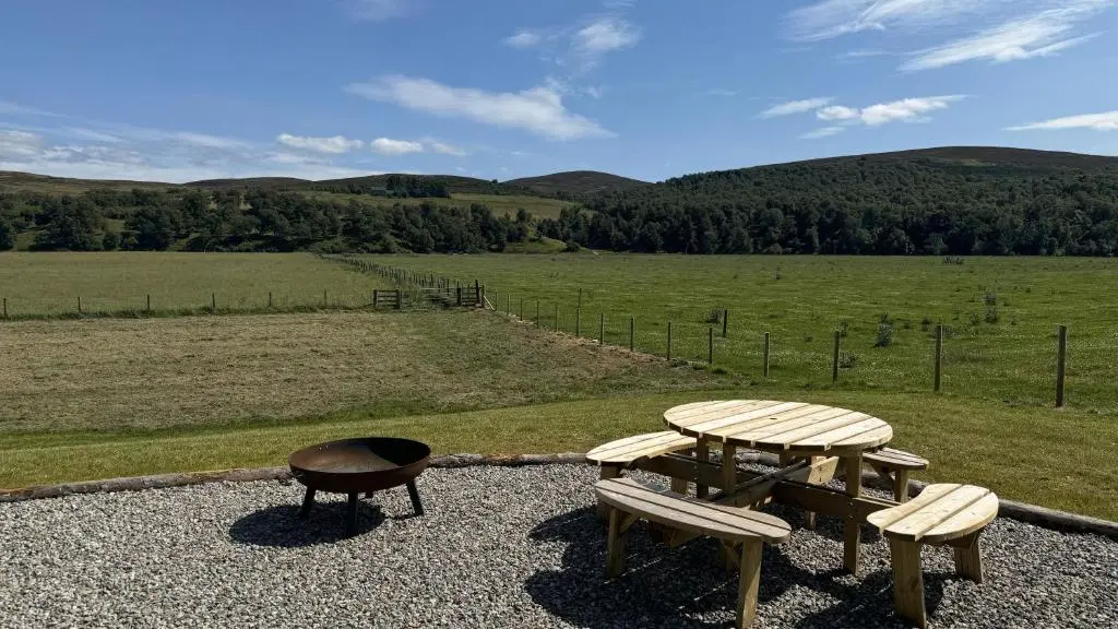 a picnic table and two benches on top of a field at Juniper Lodges in Inverness
