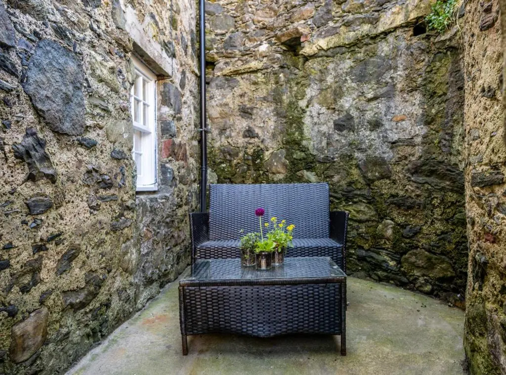 a black chair with flowers on a table in front of a stone wall at 7 Shorehead, Portsoy in Portsoy