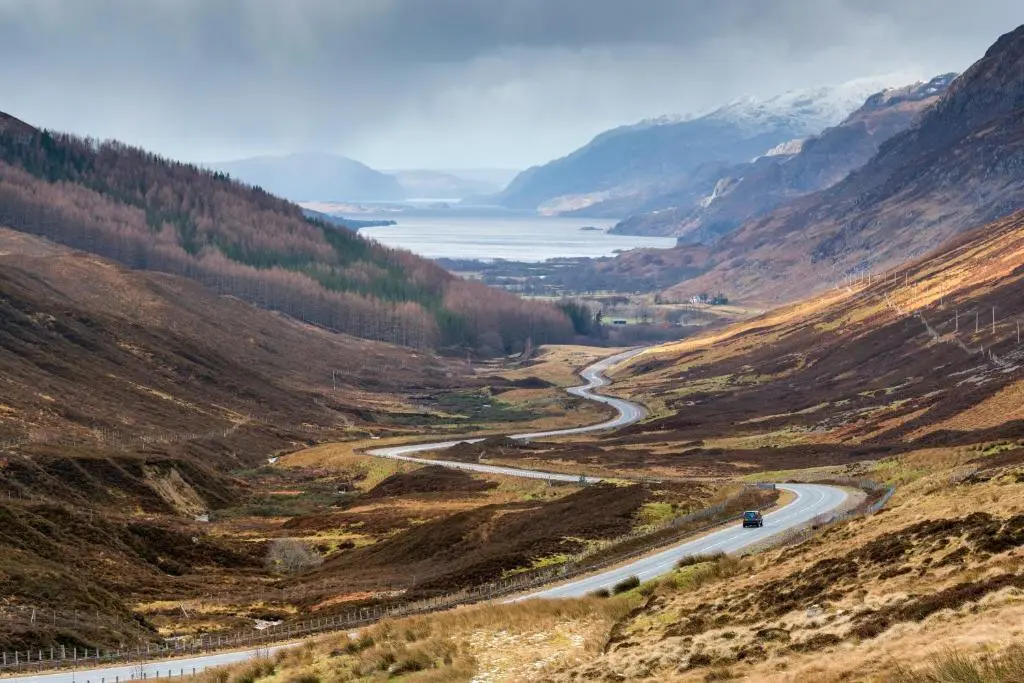 a winding road through a mountain valley with a lake at Highland Club Direct in Fort Augustus