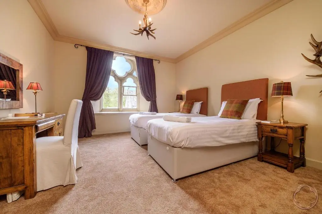 a bedroom with two beds and a desk and a window at Highland Club Direct in Fort Augustus