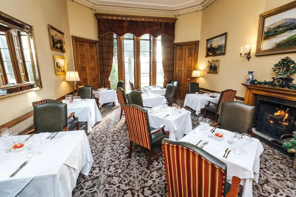 a restaurant with white tables and chairs and a fireplace at Macdonald Pittodrie House in Chapel of Garioch