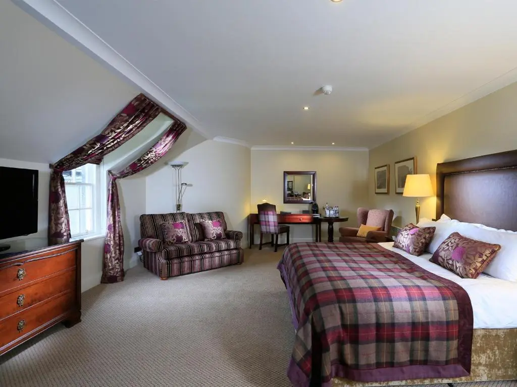 a bedroom with a bed and a couch and a television at Macdonald Pittodrie House in Chapel of Garioch