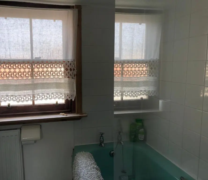 a bathroom with a green tub and two windows at A cosy seaside cottage in Cullen