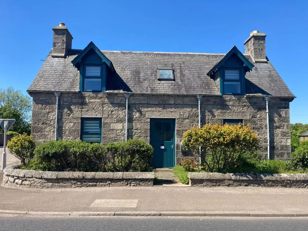 a stone house with a blue door on a street at Otago Cottage, Brora in Brora