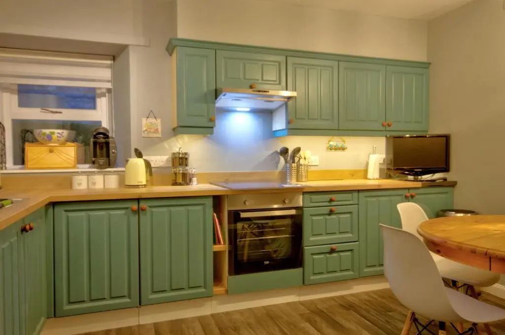 a kitchen with green cabinets and a table at Otago Cottage, Brora in Brora