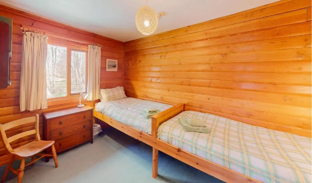 a bedroom with wooden walls and a bed and a desk at Balbeag Cottage in Insh