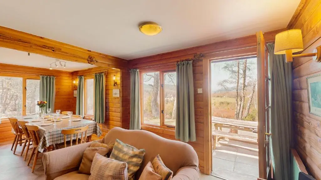 a dining room with a table and chairs and windows at Balbeag Cottage in Insh