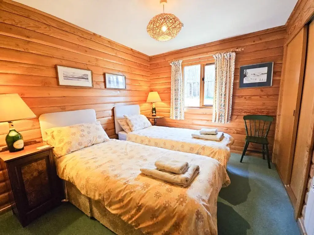 two beds in a room with wooden walls at Balbeag Cottage in Insh