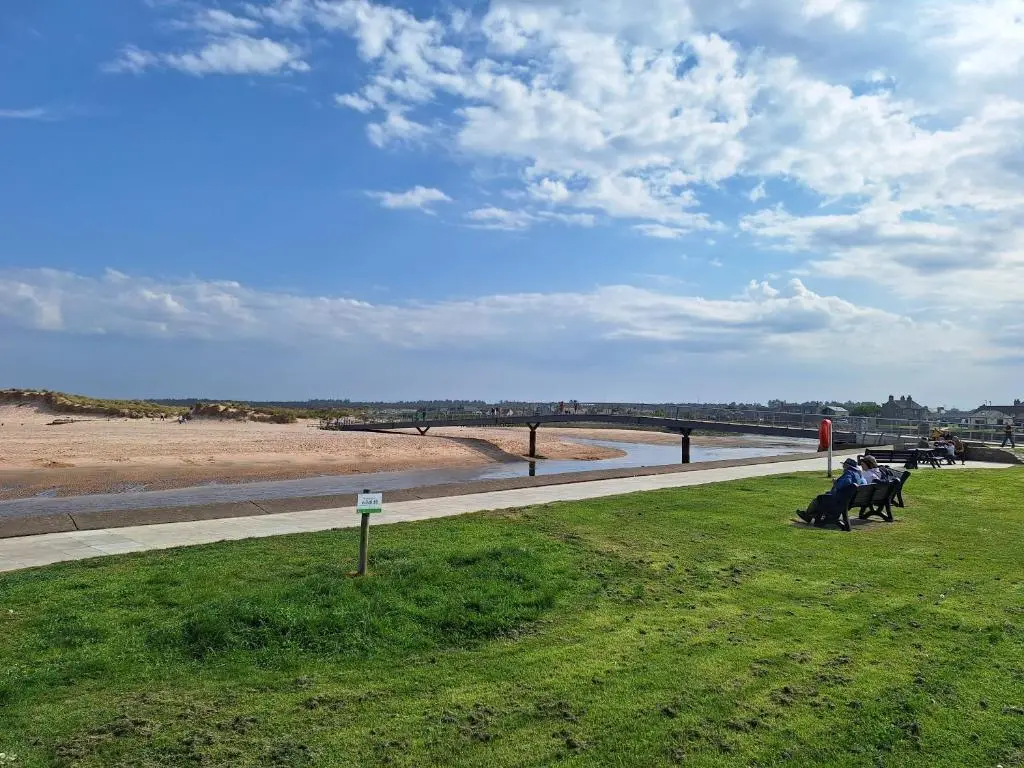 a group of people sitting in the grass near the beach at 5 Fulmar Road**Next to West Beach and Golf Course in Lossiemouth